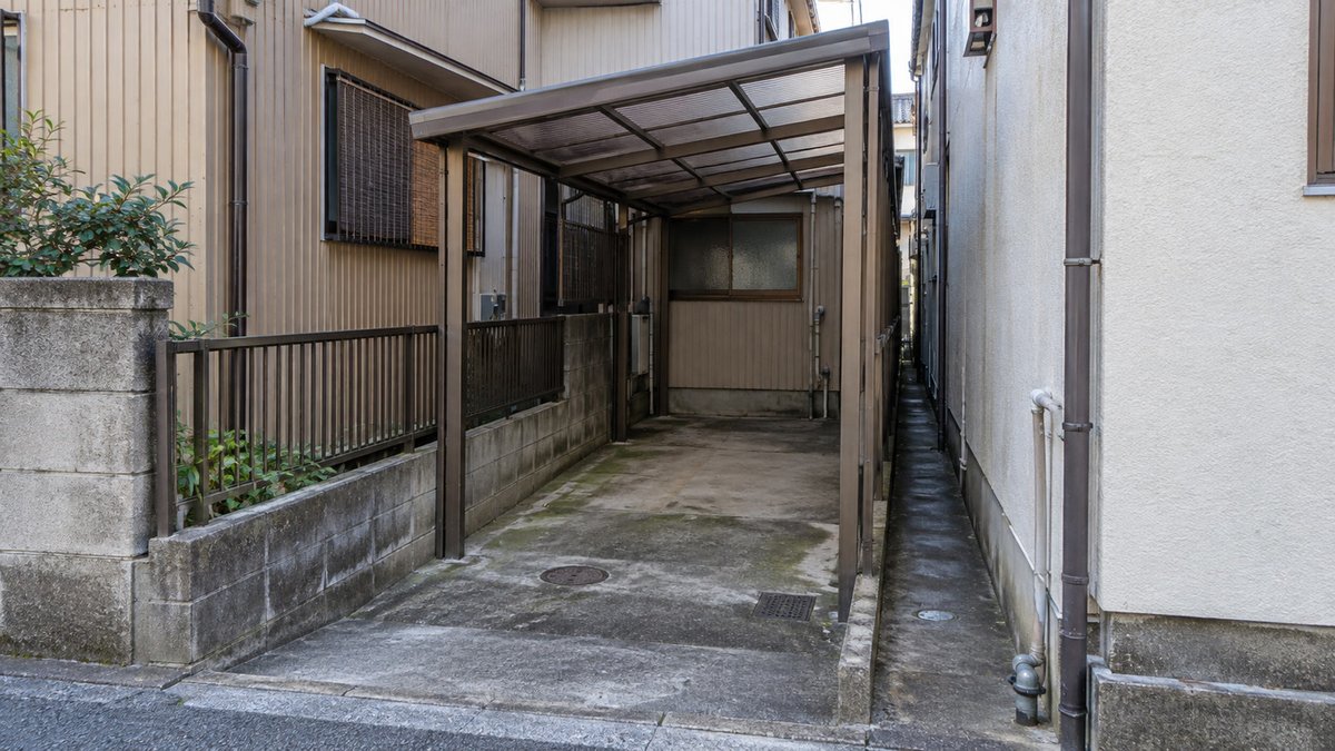 隣の家の壁ぎりぎりに建つ古いカーポート