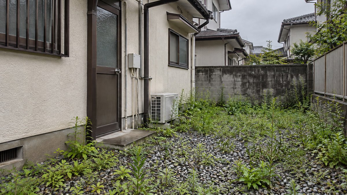 防草シートなしの砂利の間から雑草が伸びた裏庭